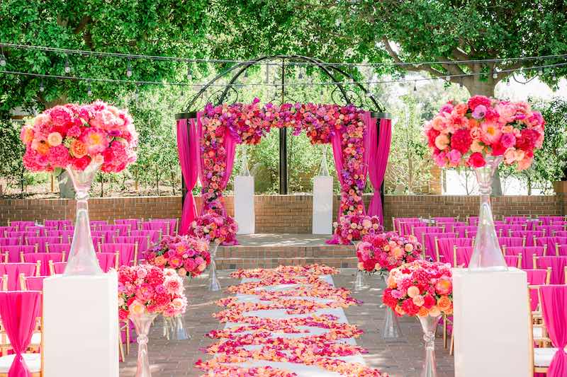In questa foto l'allestimento di un matrimonio civile stile Barbie con decorazioni floreali di colore rosa, fucsia e arancione lungo il corridoio centrale e sulla struttura dell'altare 