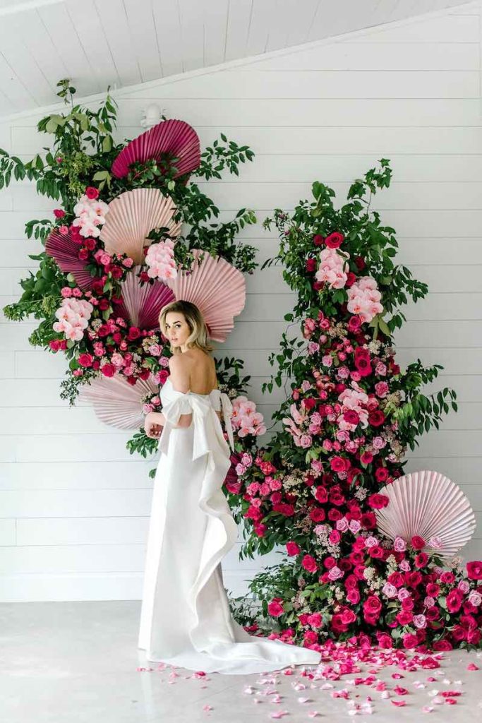 In questa foto una sposa posa davanti ad un photobooth composti di fiori di colore fucsia e rosa