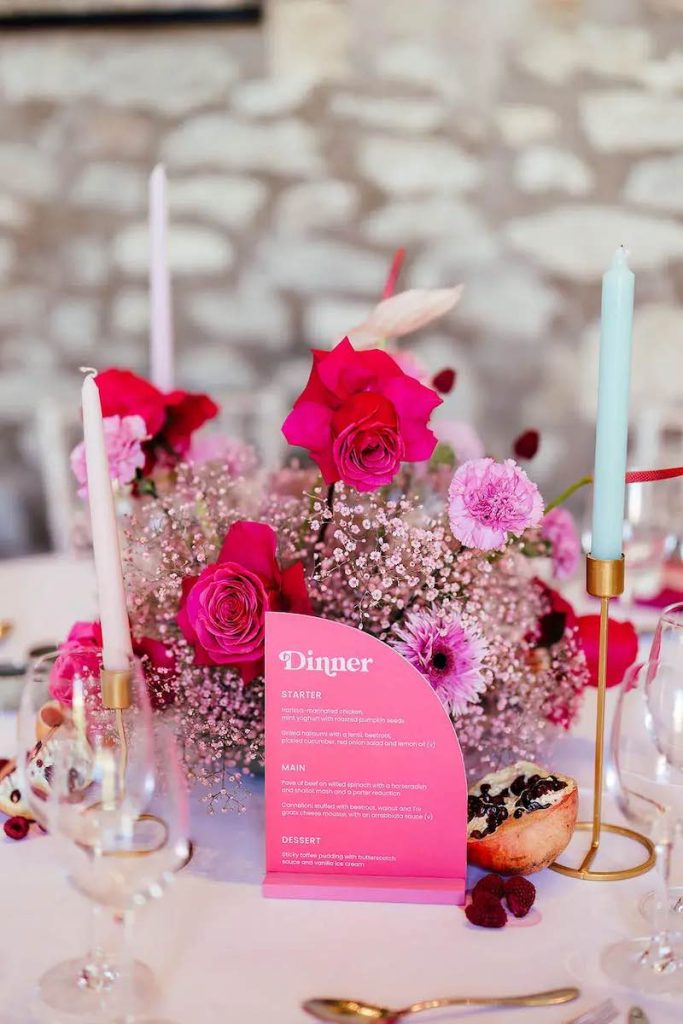 In questa foto un centrotavola composto da menù matrimonio stile Barbie di colore fucsia e fiori di colore fucsia e rosa