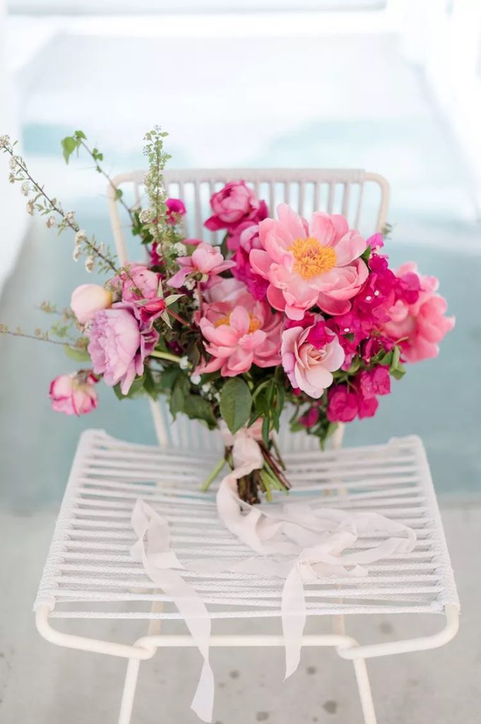 In questa foto un bouquet da sposa con fiori di colore rosa e fucsia poggiato su una sedia di colore bianco
