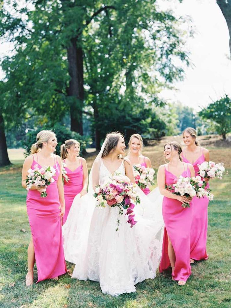 In questa foto una sposa cammina su un prato circondata dalle sue damigelle vestite con abiti lingerie di colore rosa shocking
