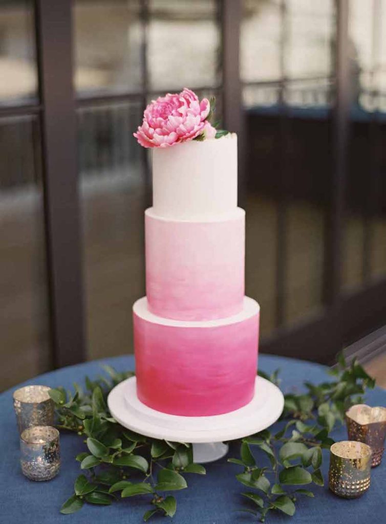 In questa foto una torta nuziale a piani con sfumatura di fucsia e rosa e con una peonia poggiata in cima