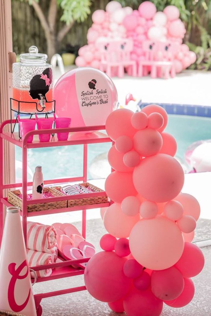 In questa foto un banchetto con bevanda, teli, flip flop e palloncini di colore rosa e fucsia