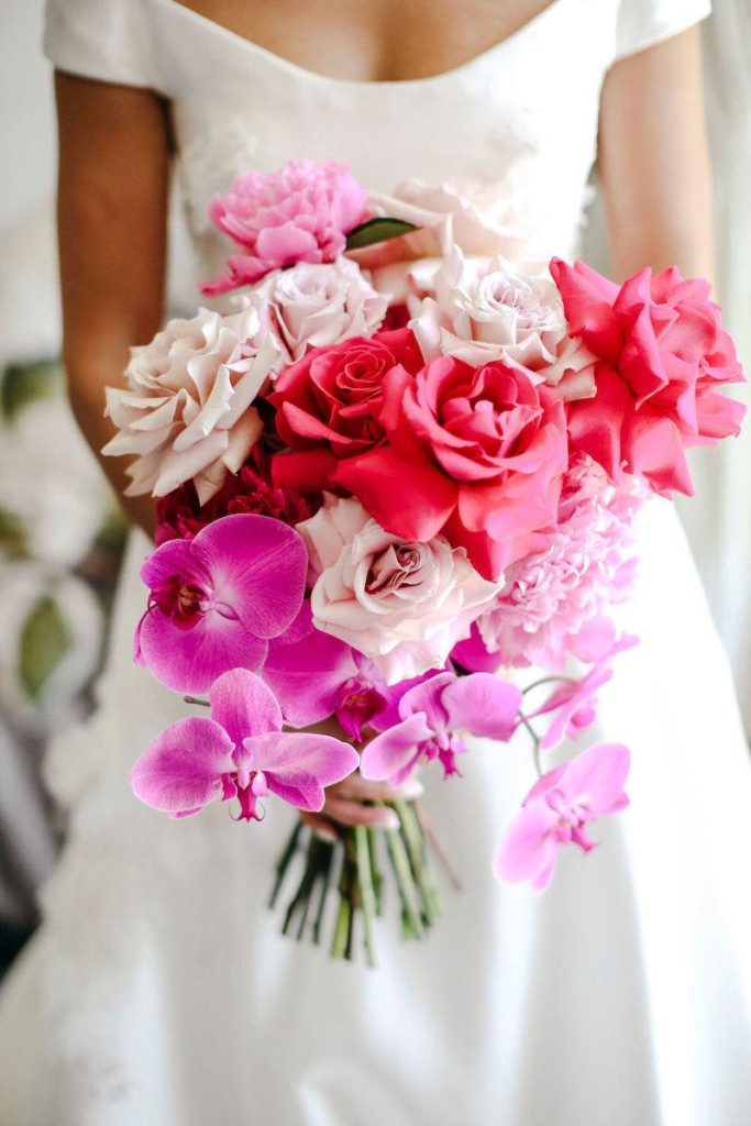 In questa foto un bouquet da sposa a cascata di rose di colore rosa e fucsia e orchidee di colore fucsia