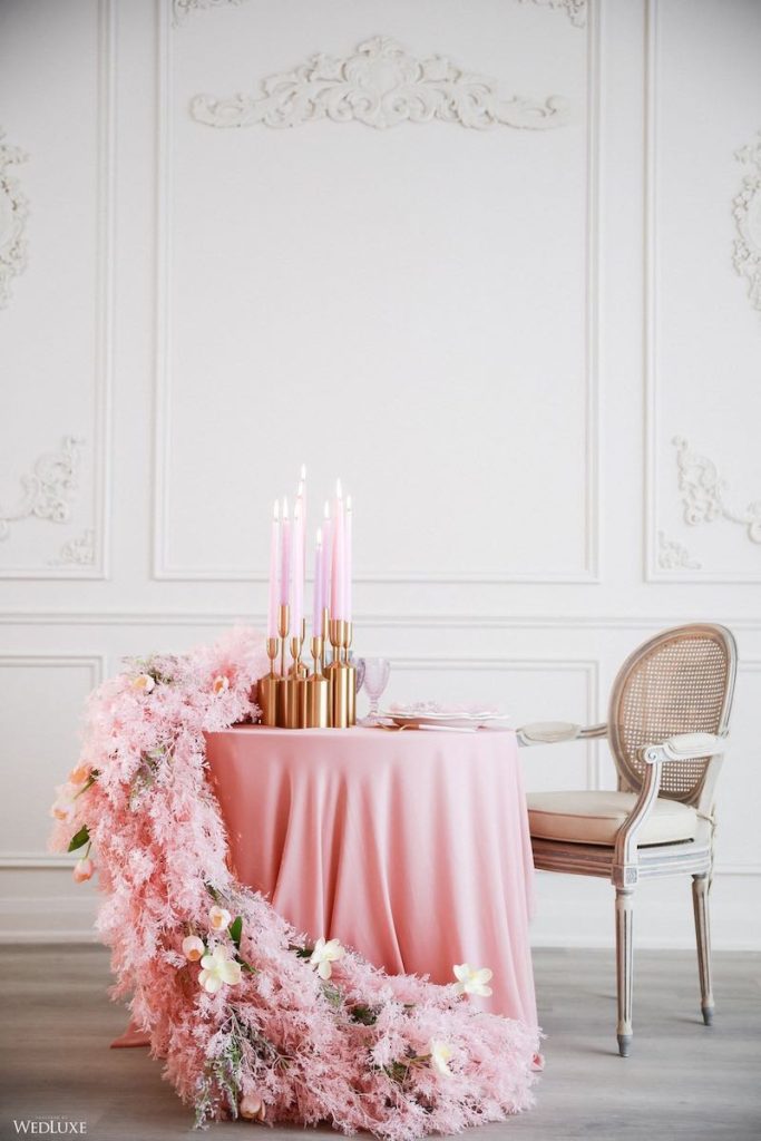 In questa foto un tavolo per matrimonio rotondo con tovaglia di colore rosa cipria, decorazione a casacata di pampas di colore rosa. Sul tavolo sono posizionate candele di colore rosa in candelabri di colore oro