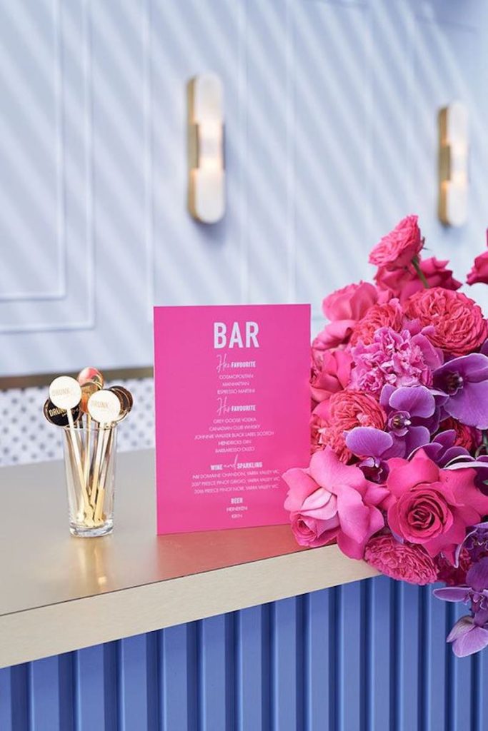 In questa foto un menù bar di colore fucsia con testo di colore bianco al fianco di fiori di colore fucsia 