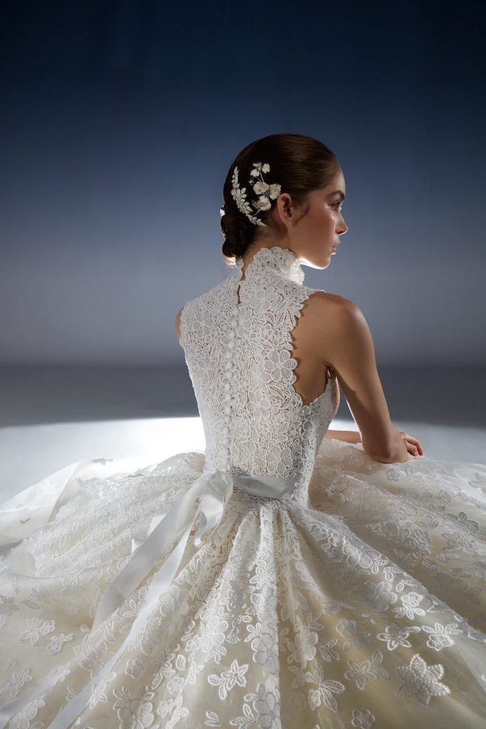 In questa foto una modella posa seduta e di spalle indossando un abito da sposa della collezione White Gold 2024 di Peter Langner 