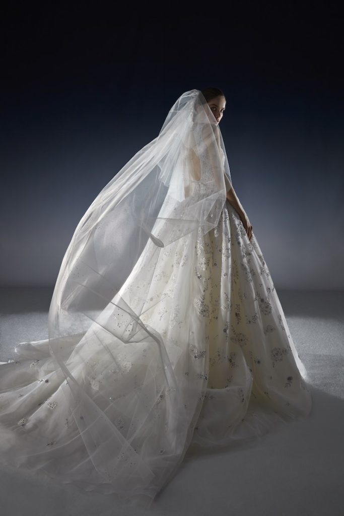 In questa foto una modella posa di spalle indossando un abito da sposa della collezione White Gold 2024 di Peter Langner in chiffon con dettagli 3D