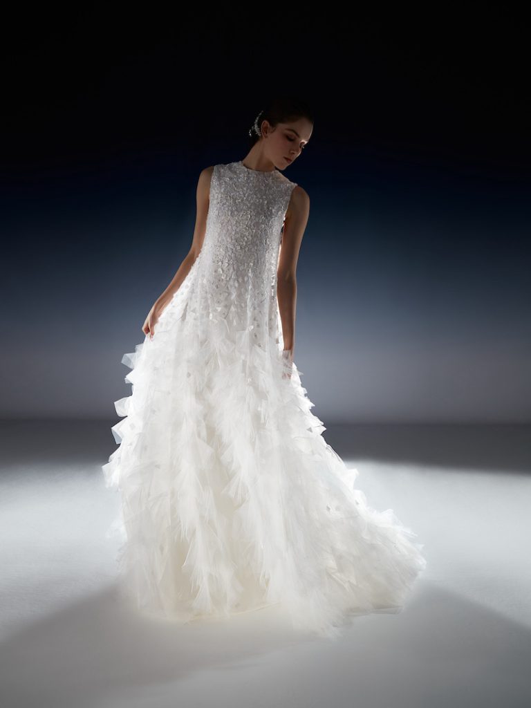 In questa foto una modella posa indossando un abito da sposa della collezione White Gold 2024 di Peter Langner con scollatura girocollo e petali 3D