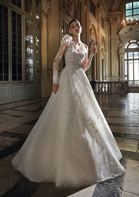 In questa foto una modella indossa un abito da sposa Pronovias Privée 2024 monospalla, con ricami floreali lungo la manica, il corpetto e la parte alta della gonna ad A
