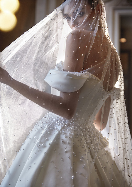 In questa foto una modella mostra un velo tempestato di perline bianche: è uno degli accessori che completano il look sposa Pronovias Privée 2024