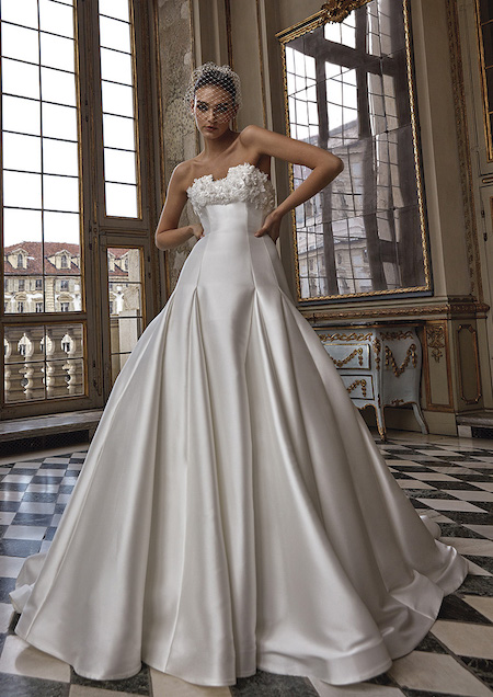In questa foto un abito da sposa Pronovias Privée 2024 dal taglio Fit & Flare. Fiori 3 D adornano lo scollo retto del vestito