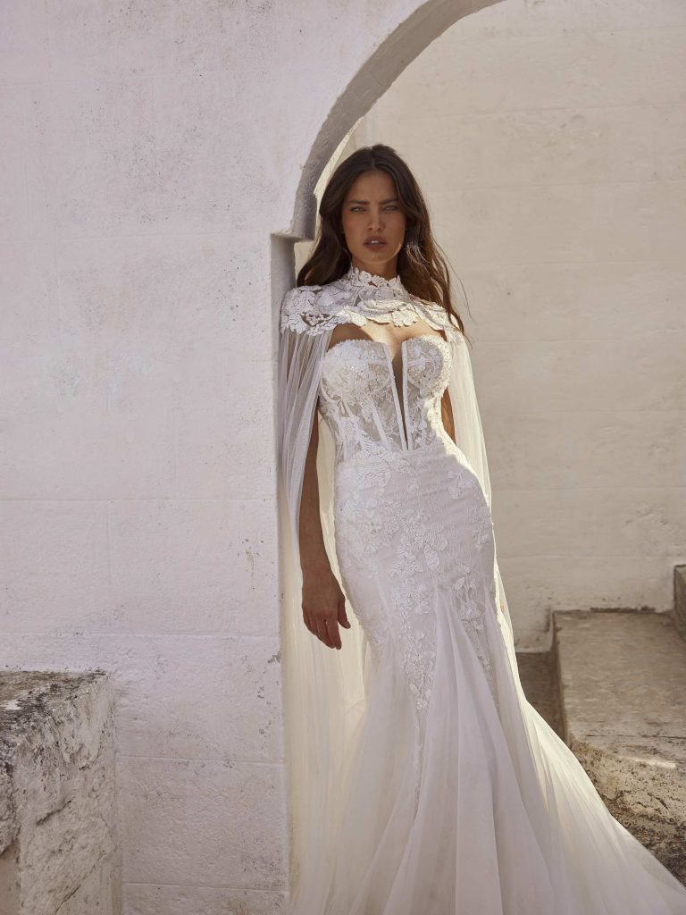 In questa immagine un abito da sposa Capri 2024 a sirena con mantella ricamata. 