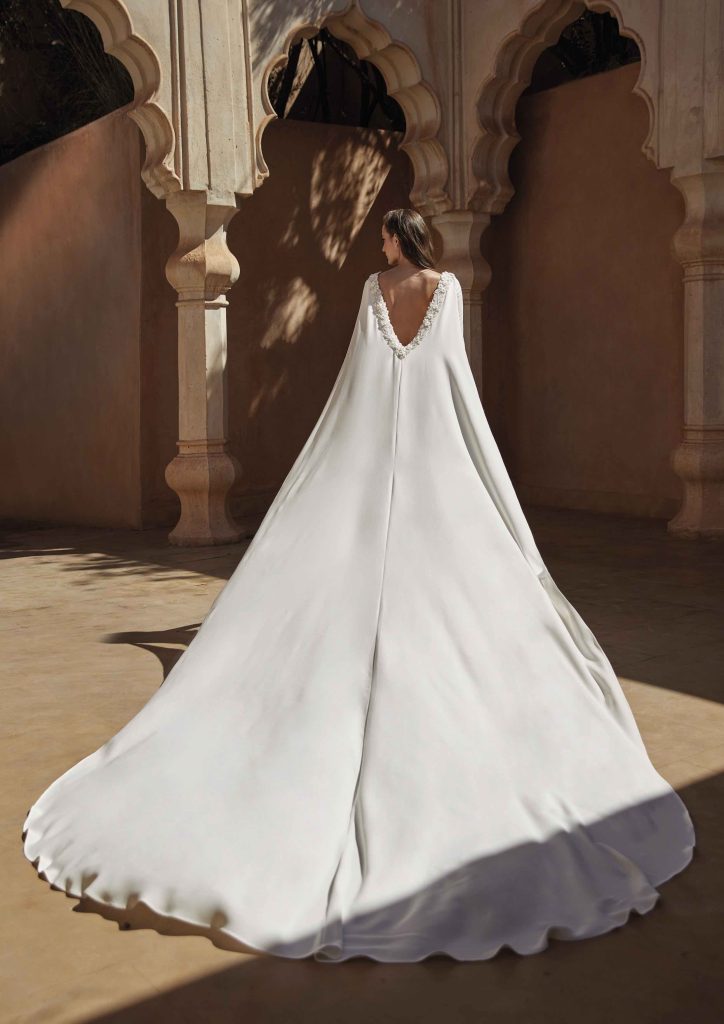 In questa immagine un abito da sposa con una mantella lunghissima. 