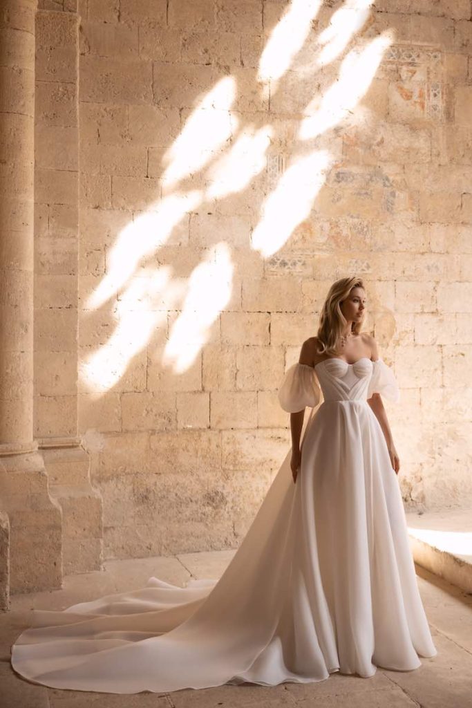 In questa foto una modella posa indossando uno degli abiti da sposa romantici 2024 di Eva Lendel con gonna ad A in chiffon, scollo a cuore e maniche balloon removibili 