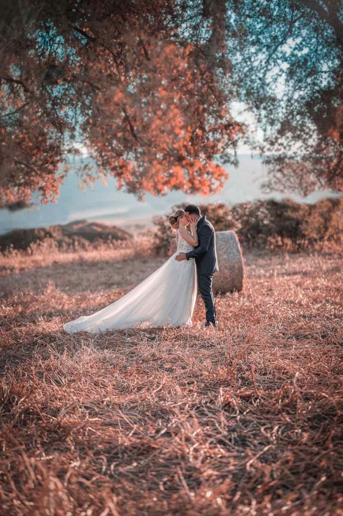 In questa foto di Virgilio Ferrara due sposi si baciano su un campo di grano circondati a alberi e da balle di fieno