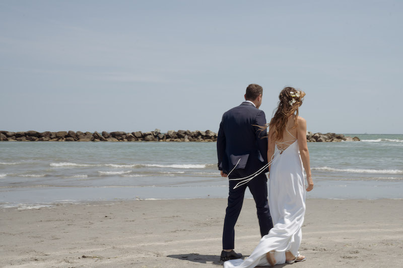 In questa foto due sposi di spalle mentre camminano su una spiaggia