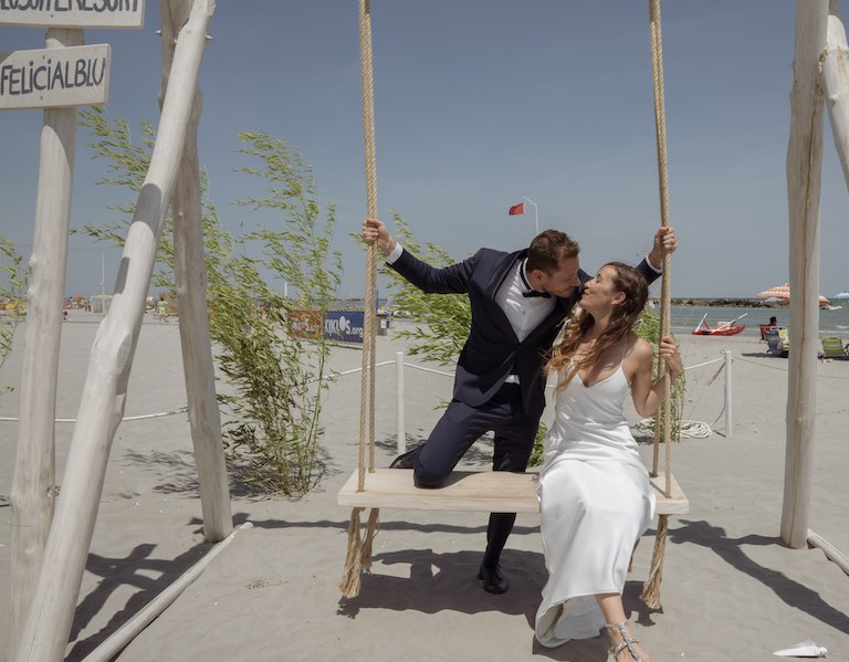 In questa foto due sposi si baciano su un'altalena dopo il loro matrimonio sulla spiaggia del Blu Suite Resort