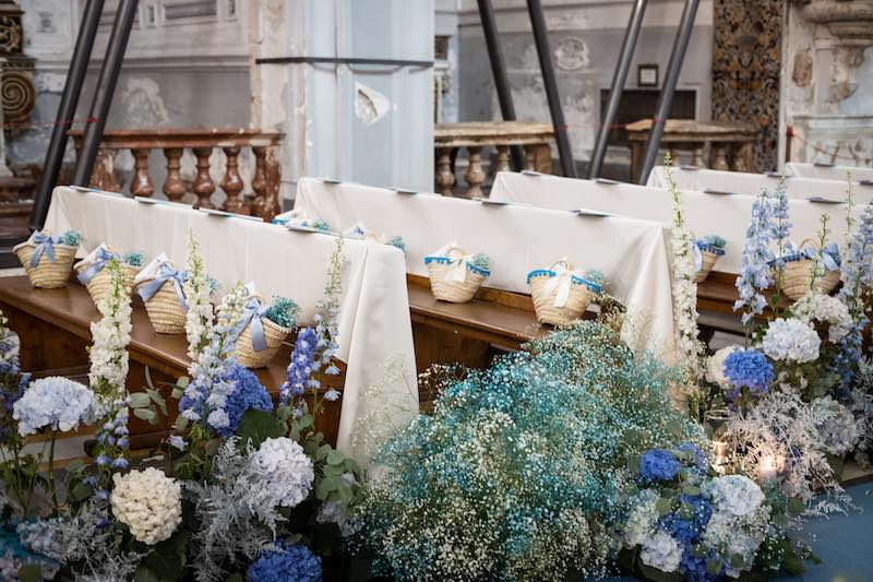 In questa foto l'allestimento dei banchi di una chiesa per un matrimonio organizzato da Jenny Scalera. Attorno ai banchi sono presenti composizioni nei toni del blu mentre sui banchi sono adagiate coffe usate come Wedding Bag 