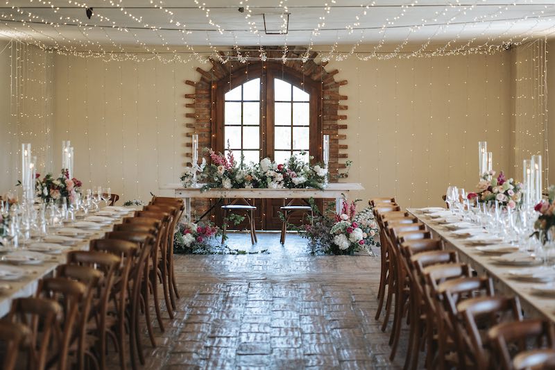 In questa foto l'allestimento di un matrimonio nella sala interna di Tenuta Corte Vittoria con tavoli imperiali e fiori di colore rosa e bianchi