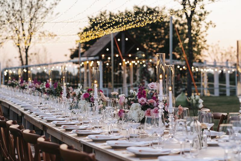 In questa foto una mise en place in stile romantico con fiori rosa e fucsia allestita su un tavolo imperiale nel giardino di Tenuta Corte Vittoria