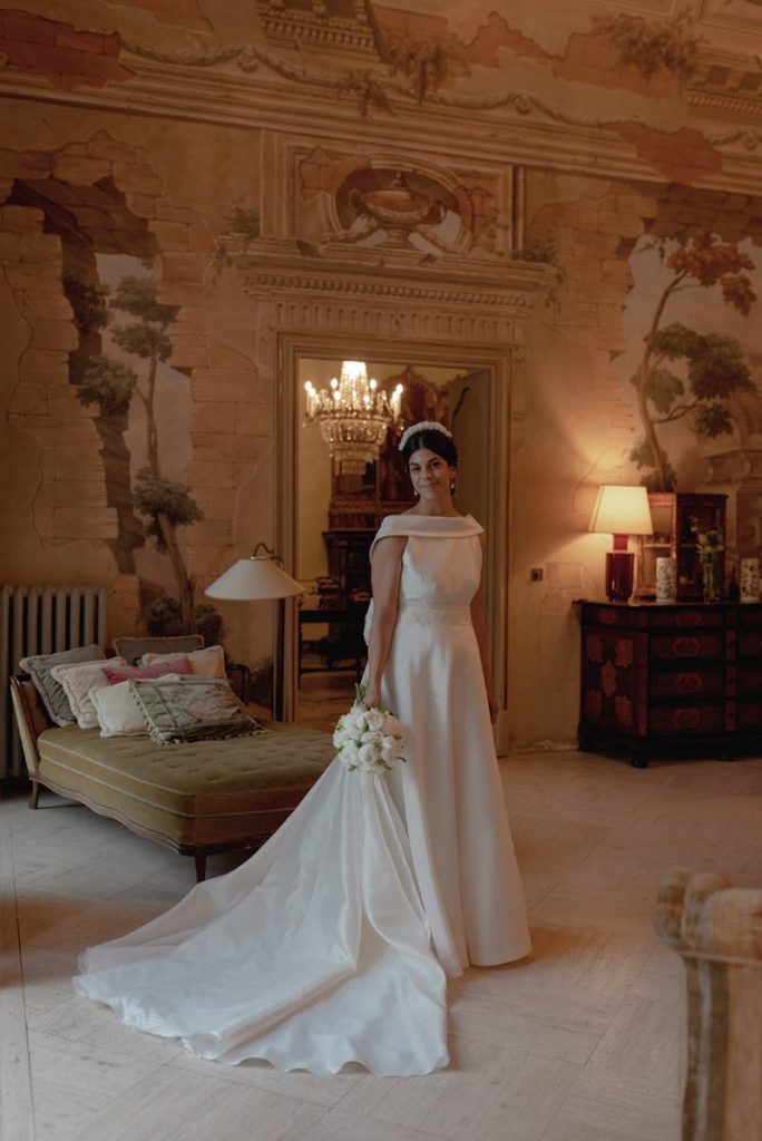 In questa foto la sposa Elena Natoli posa in uno dei saloni di Villa Tasca a Palermo. La sposa tiene nella mano destra un bouquet di peonie bianche