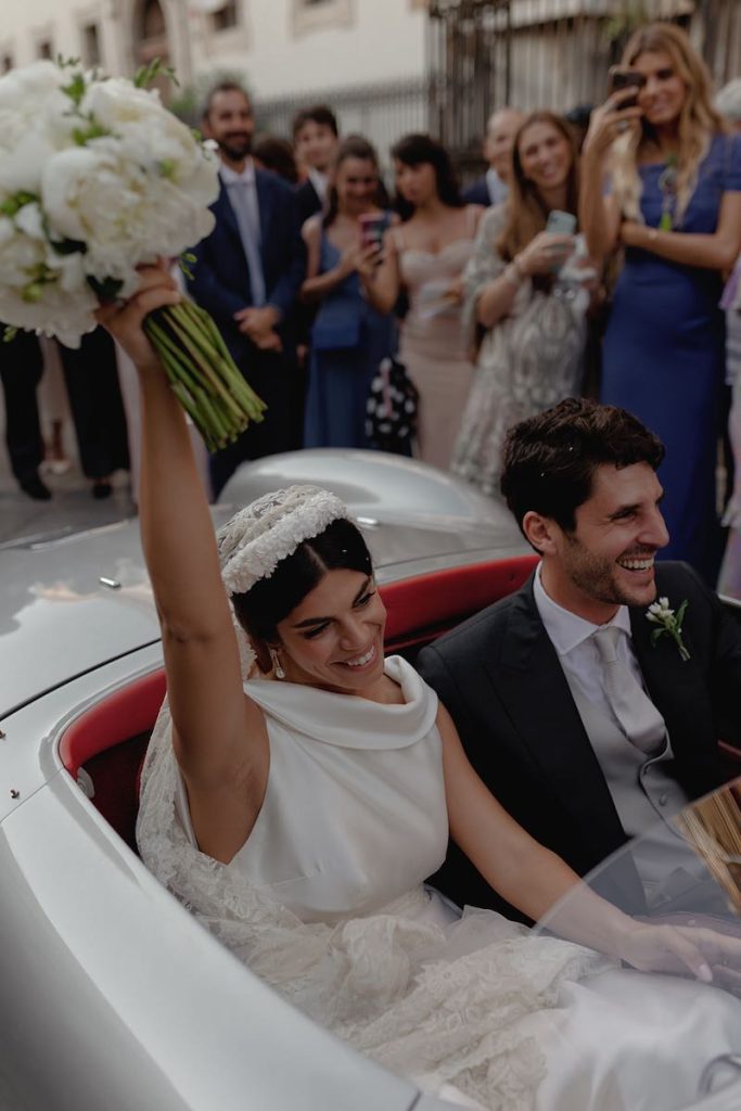 In questa foto gli sposi Elena e Nicola a bordo di una Porsche vintage grigio perla. Elena solleva il suo bouquet in alto