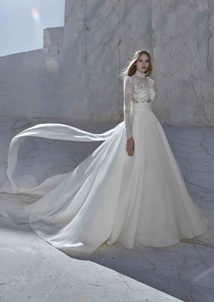 In questa immagine un abito da sposa da principessa 2024 con corpetto in pizzo con maniche lunghe e gonna in seta di Atelier Pronovias.