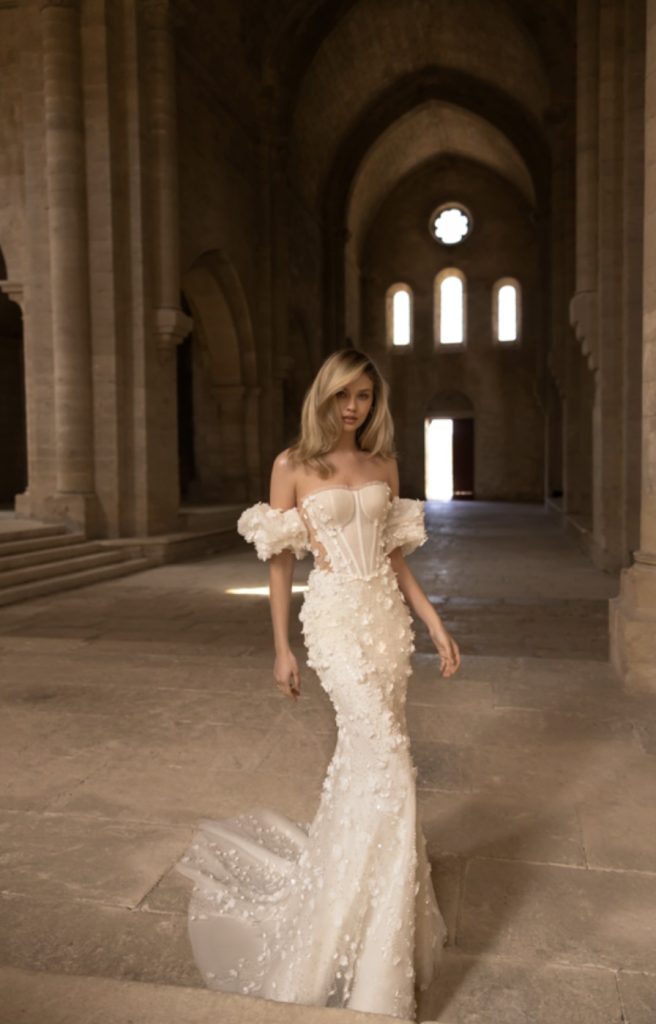 In questa immagine un vestito da sposa s sirena con dettagli floreali in 3D in tutto il modello. 