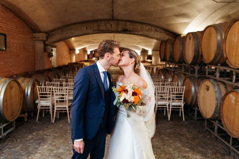In questa foto gli sposi Enrica e Davide si baciano sullo sfondo della barricaia di Tenuta Carretta dove è stato celebrato il loro matrimonio simbolico