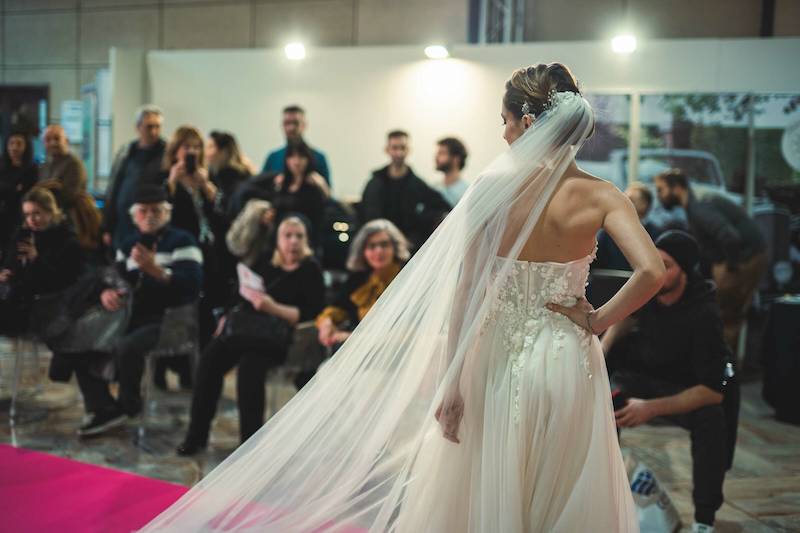 In questa foto una modella di spalle sfila a Bergamo indossando un abito da sposa con velo abbinato a Bergamo Sposi