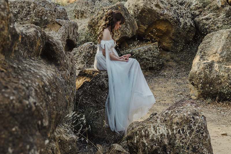 In questa foto di Alessandro Tondo una sposa seduta su uno roccia guarda la sua fede al dito