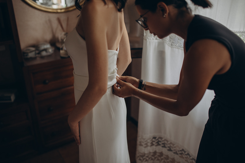 In questa foto la Bridal Stylist Giulia Solli chinata in avanti sistema il retro di un abito su una sposa 