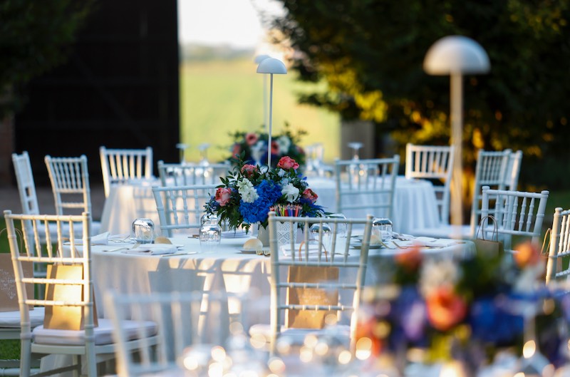 In questa foto tavoli per matrimonio di forma rotonda allestiti con tovagliato bianco e centrotavola di colore blu, rosa, bianco e arancione