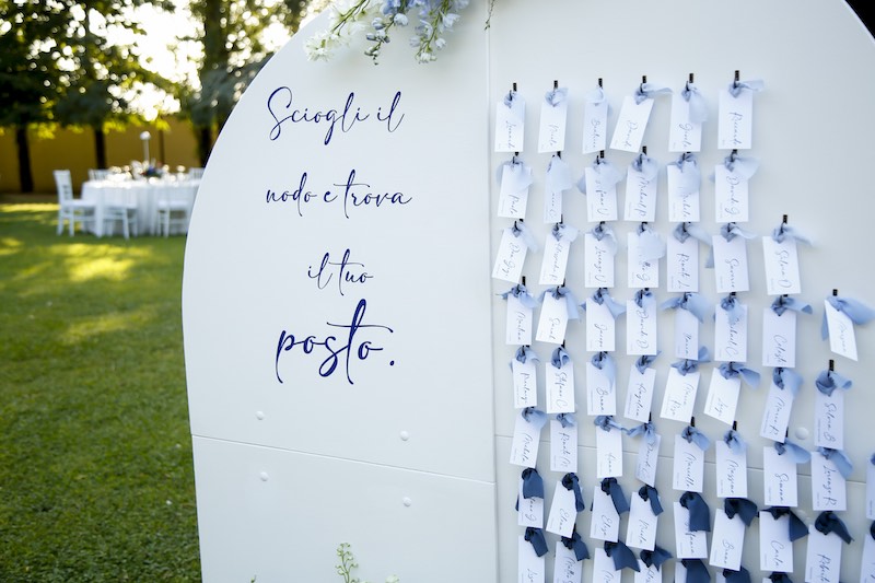In questa foto una tableau de mariage nelle tonalità del blu e del turchese realizzato dalla Wedding Planner Romina Pecorari con scritto: "Sciogli il nodo e trova il tuo posto"