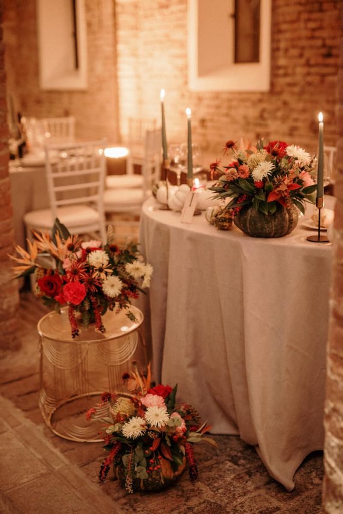 In questa foto il dettaglio della decorazione del tavolo degli sposi Silvia e Alessandro decorato da OttoQuattro Eventi con tavoli in ferro di colore oro con piano in vetro e composizioni di rose, anthurium, sterlizia, nutan, garofani disposti all'interno di zucche