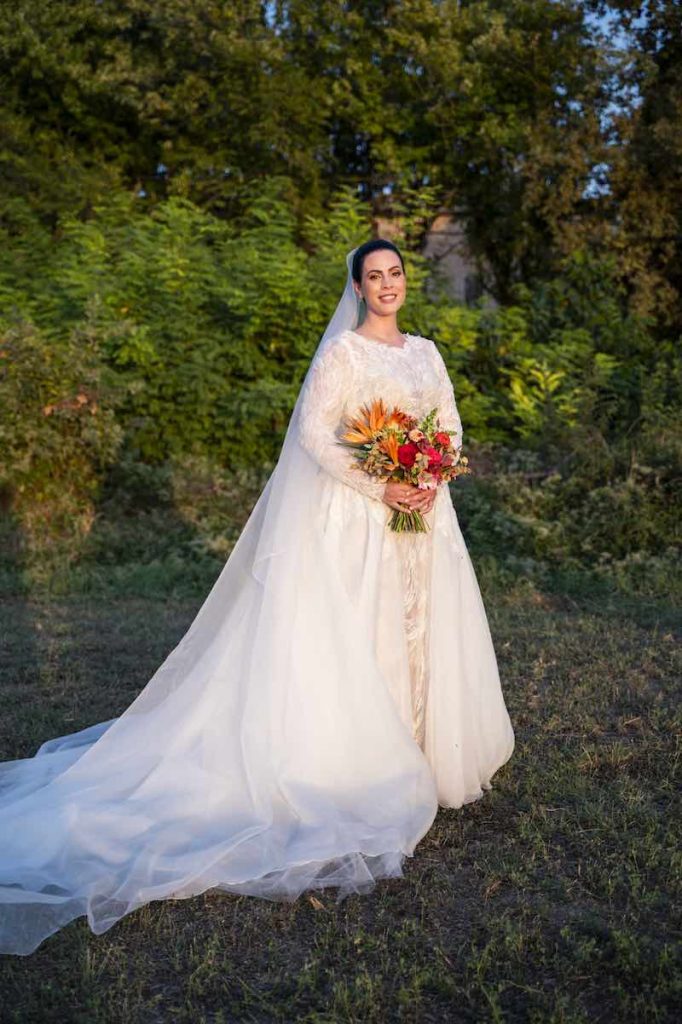 In questa foto la sposa Silvia posa nel parco di Corte Ortalli con il suo bouquet e indossa un abito da sposa ricamato e con sopragonna removibile