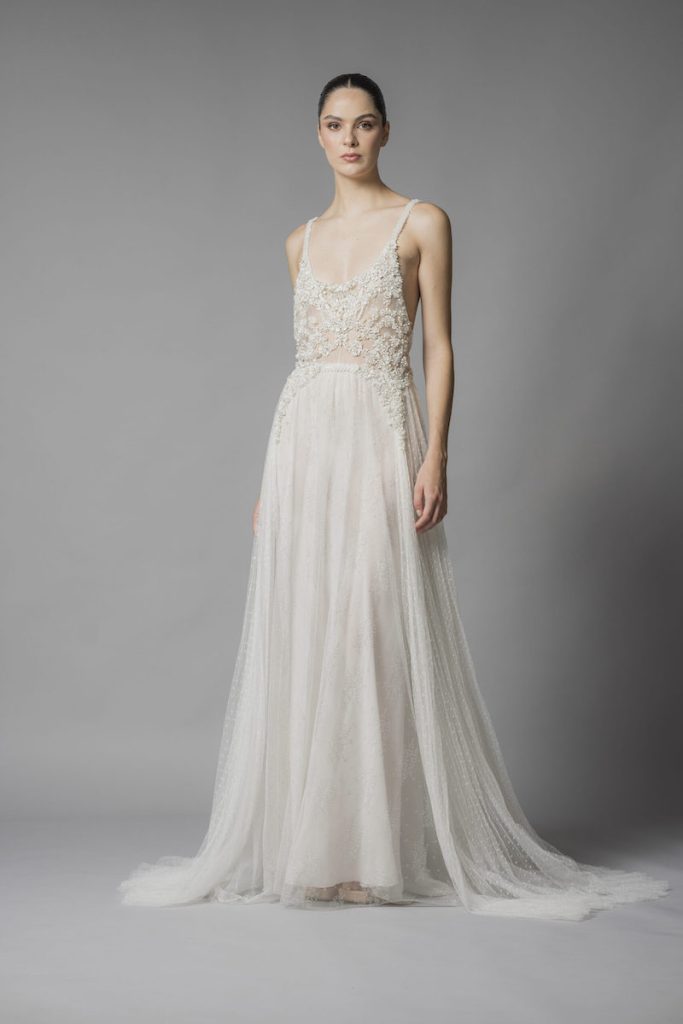 In questa foto una modella posa indossando un abito da sposa scivolato in tulle plumetis e ricami di perline sul corpetto di Marco y Maria