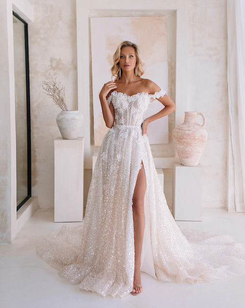 In questa foto una modella indossa un abito da sposa romantico 2024, tempestato di micro paillettes lucenti e spacco sulla gamba, firmato Agnieszka Swiatly