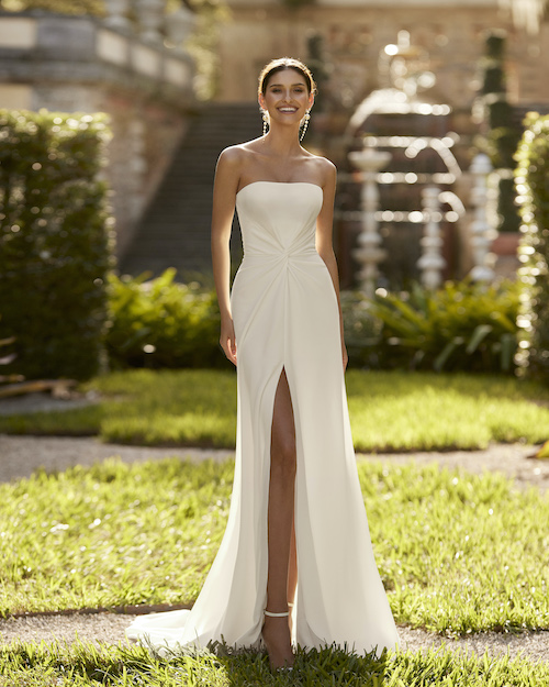 In questa foto una modella indossa uno degli abiti da sposa con spacco 2024 più semplici: si tratta di un modello di Aire Barcelona, impreziosito da un drappeggio sul punto vita