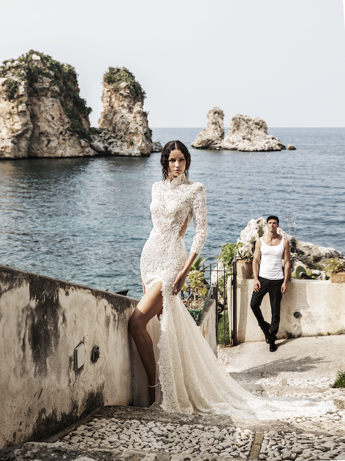 In questa foto una modella posa davanti ai faraglioni di Capri indossando una sirena in pizzo all over, con spacco a metà coscia, dello stilista Alessandro Angelozzi per il 2024