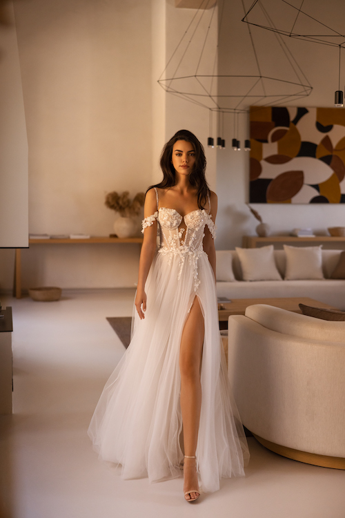 In questa foto una modella cammina indossando un romantico vestito da sposa 2024, con spacco, di Elizabeth Passion