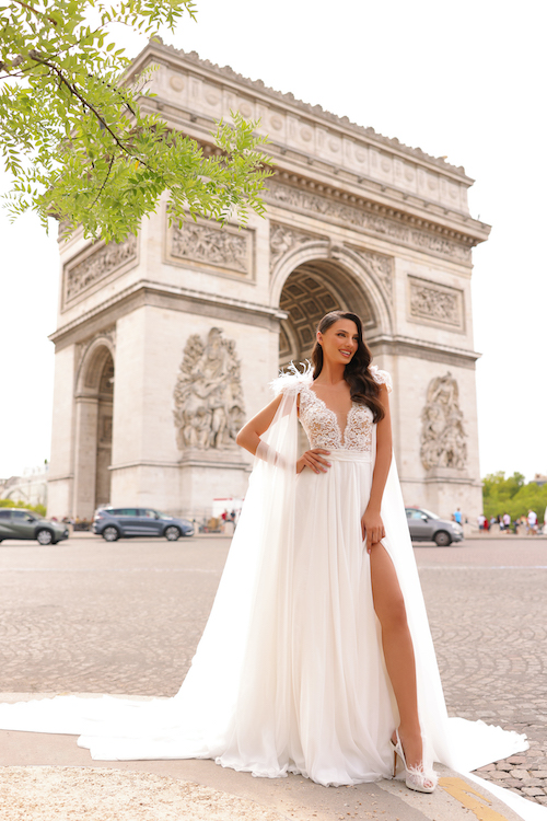 In questa foto una modella posa davanti all'Arco di Trionfo, a Parigi, indossando un vestito da sposa con spacco 2024 della stilista Michela Ferriero