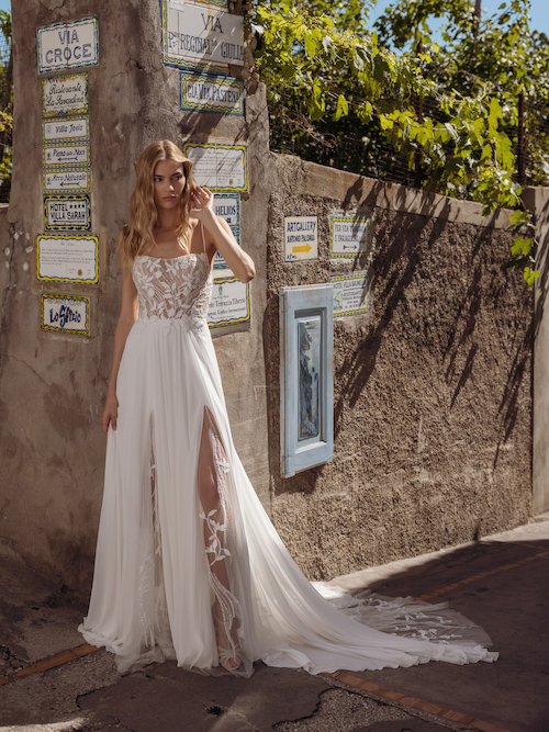 In questa foto una modella posa con uno degli abiti da sposa con spacco 2024 di Modeca: l'abito è scivolato, con le bretelle super sottili, e il corpetto con un foliage ricamato