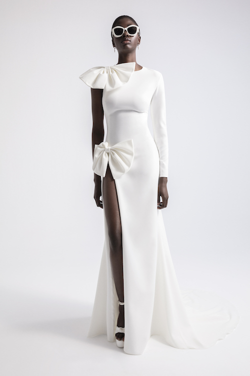 In questa foto una modella posa con uno degli abiti da sposa con spacco 2024 più hot: il vestito di YolanCris ha un'apertura vertiginosa sulla coscia e due maxi fiocchi applicati sulla spalla e sull'anca