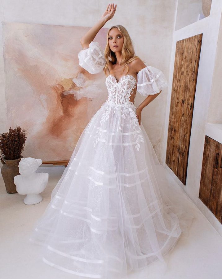 In questa foto una modella indossa un abito da sposa ad A Agnieszka Swiatly 2024 in tulle a righe con maniche balloon staccabili e ramage di foglie che scendono dal busto