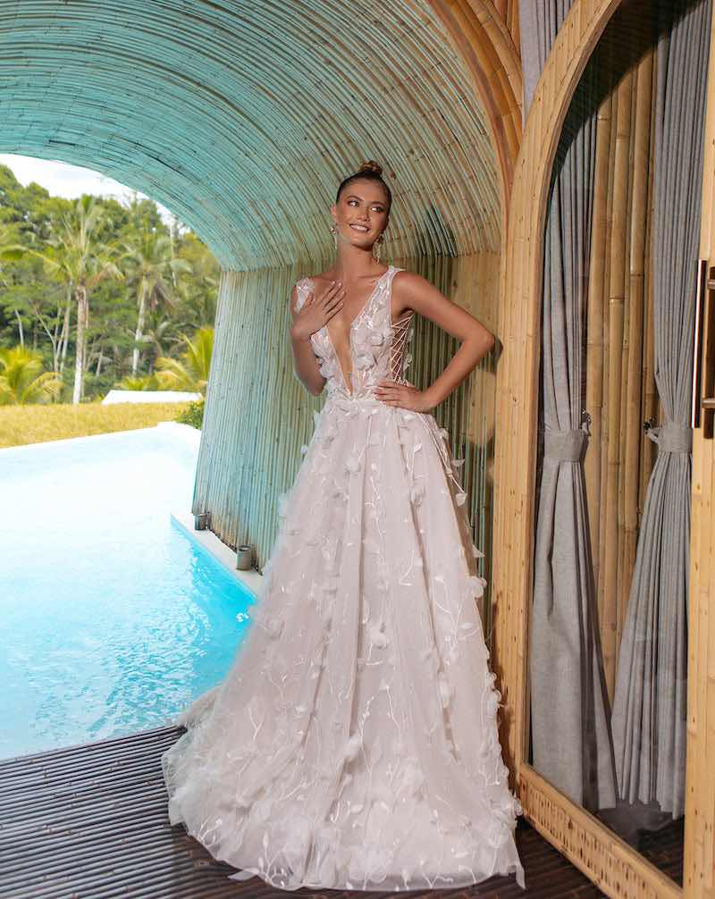 In questa foto una modella posa indossando un abito da sposa Agnieszka Swiatly 2024 con gonna ad A, scollo a V e fiori 3D