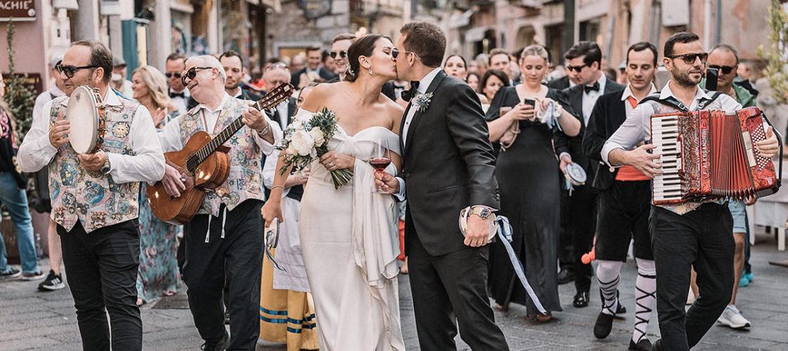 Una coppia di sposi in Sicilia si bacia con attorno familiari, amici e la banda: la foto è stata realizzata da Antonino Gitto, fotografo di matrimonio in Sicilia