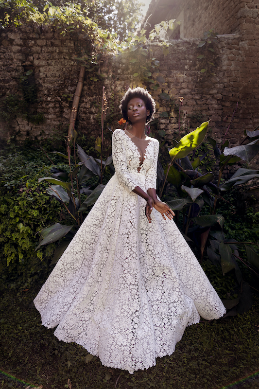 In questa foto una modella indossa un abito da sposa in pizzo guipure all over, con profonda scollatura a V sul décolleté, maniche tre quarti e gonna scivolata, di Andrea Sedici 2024 