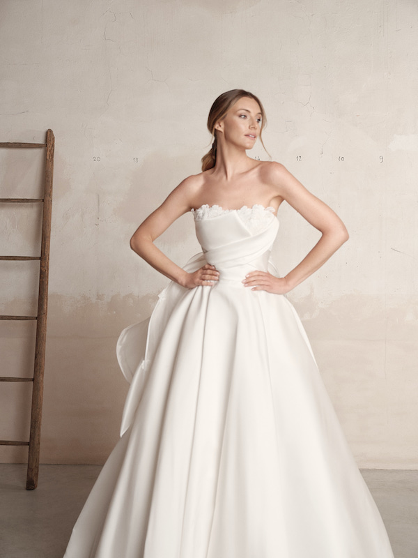 In questa foto una modella posa con un abito da sposa con corpetto drappeggiato di Creazioni Maria Pia 2024